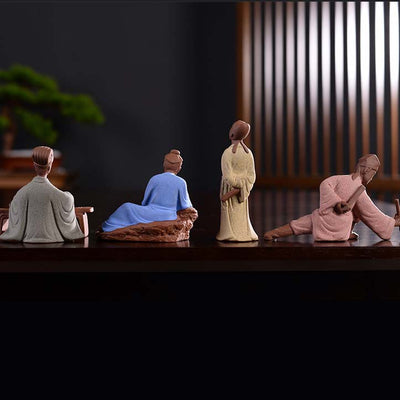 4 statues chinoises personnages historiques Zhuge Liang Lu Yu Li Bai Tang Yin vue de dos posées sur une table en bois laqué sombre avec un fond flou Kaosix
