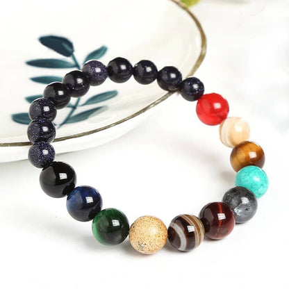 Bracelet Système Solaire avec 11 Planètes en Perles de Pierres posé sur le rebord d'une assiette blanche Kaosix