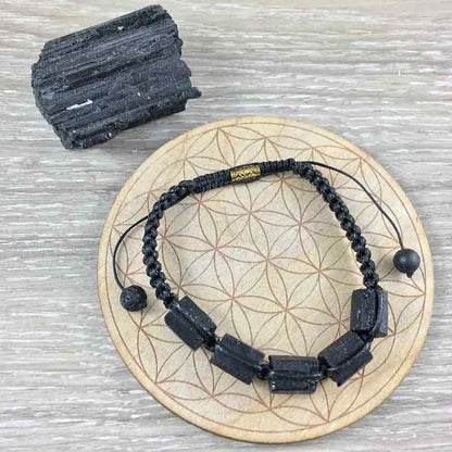 Bracelet “énergie” en tourmaline noire et macramé sur une planche en bois posée à côté d'un morceau de tourmaline Kaosix