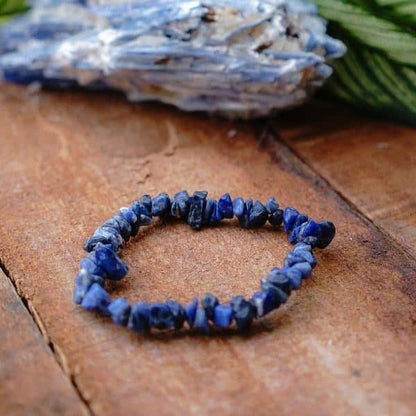 Bracelet baroque (chips) lapis-lazuli sur le bras posé sur une planche en bois et à coté d'un rocher gris Kaosix