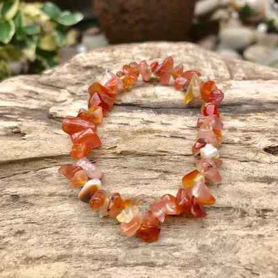 Bracelet baroque chips agate rouge sur un gros rocher gris en extérieur dans un jardin kaosix