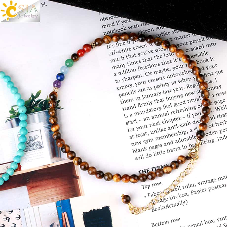 Bracelet de cheville 7 chakras et œil de tigre posé sur un livre Kaosix