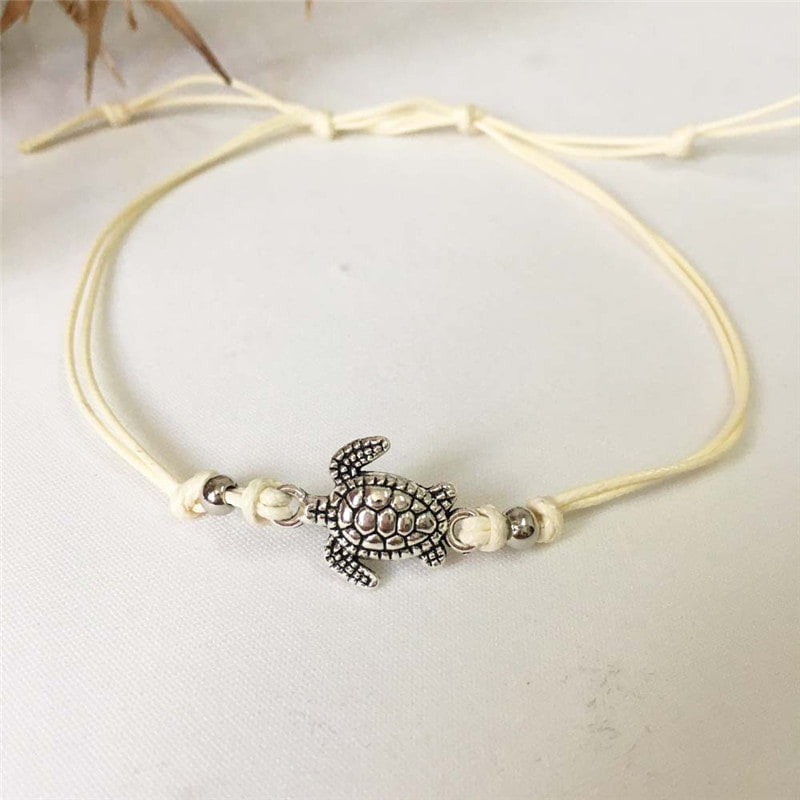 Bracelet de cheville avec amulette tortue de mer en métal argenté et cordon blanc sur une nappe blanche Kaosix