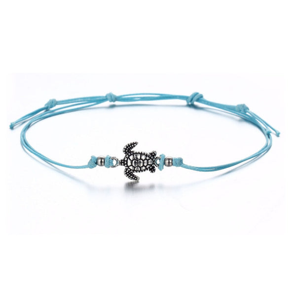 Bracelet de cheville avec amulette tortue de mer en métal argenté et cordon bleu sur fond blanc Kaosix