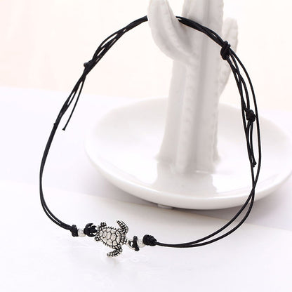 Bracelet de cheville avec amulette tortue de mer en métal argenté et cordon noir sur socle blanc Kaosix
