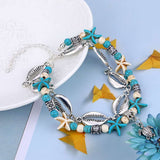 Bracelet de cheville en coquillages cauris étoiles de mer avec amulette tortue de mer sur une assiette blanche et une table bleue Kaosix