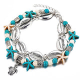 Bracelet de cheville en coquillages cauris étoiles de mer avec amulette tortue de mer sur un sol blanc Kaosix