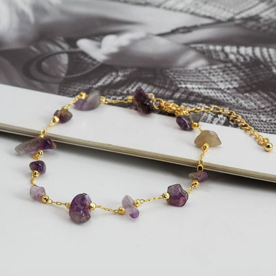 Bracelet de cheville en éclats de pierre d’améthyste et chaînette dorée sur une table blanche Kaosix