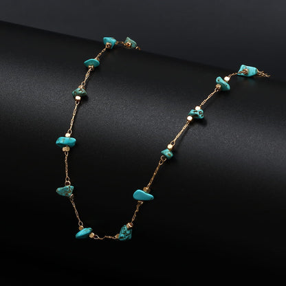 Bracelet de cheville en éclats de pierre turquoise et chaînette dorée posé sur un support noir Kaosix