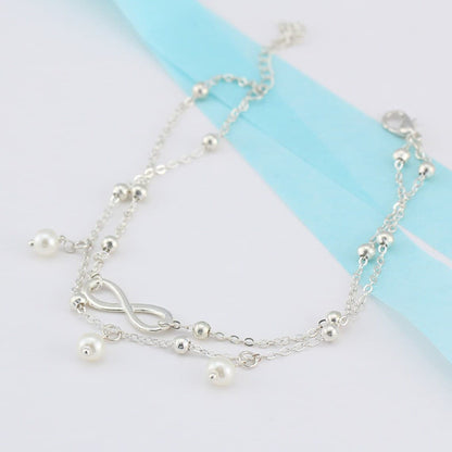 Bracelet de cheville infini et perles chainette argentée sur une nappe grise Kaosix