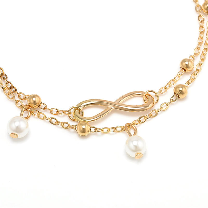 Bracelet de cheville infini et perles chainette dorée sur un nappe blanche et vue en gros plan sur l'amulette symbole infini Kaosix