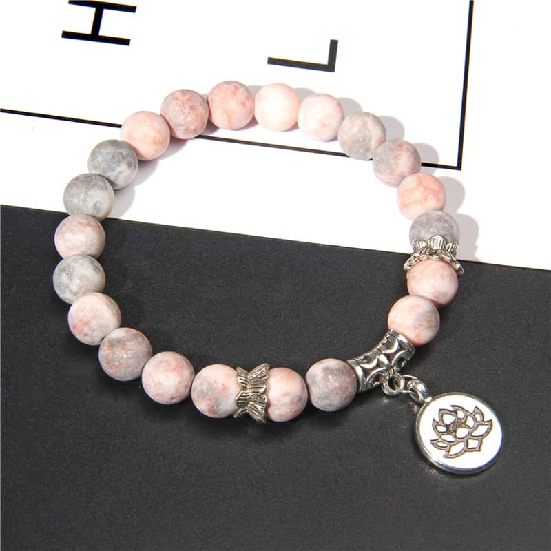 Bracelet en jaspe rose et sa breloque fleur de lotus sur une table grise foncée Kaosix