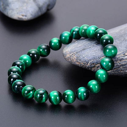 Bracelet en œil de tigre vert énergisant posé sur une pierre grise et une table noire Kaosix