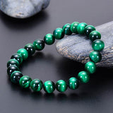 Bracelet en œil de tigre vert énergisant posé sur une pierre grise et une table noire Kaosix