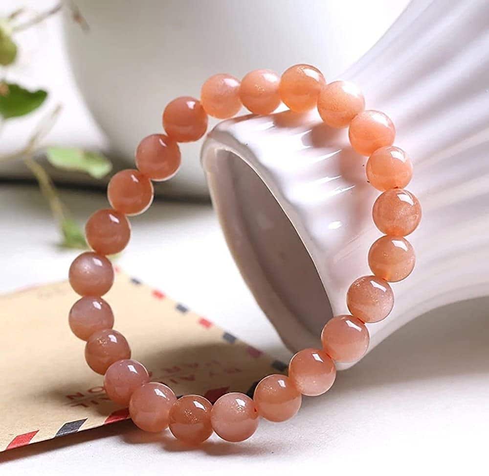 Bracelet en pierre de soleil énergie posé contre un vase blanc sur une table Kaosix