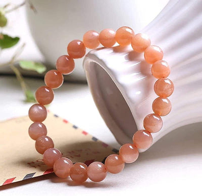 Bracelet en pierre de soleil énergie posé contre un vase blanc sur une table Kaosix