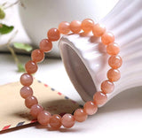 Bracelet en pierre de soleil énergie posé contre un vase blanc sur une table Kaosix