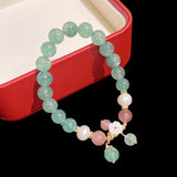 Bracelet en quartz fraise, quartz vert et quartz blanc posé sur le rebord d'une petite boite rouge et blanche Kaosix
