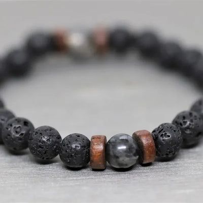 Bracelet homme en pierre de lave et en pierre de lune noire posé sur un sol gris et flouté Kaosix