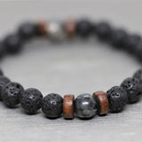 Bracelet homme en pierre de lave et en pierre de lune noire posé sur un sol gris et flouté Kaosix