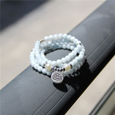 Bracelet mala 108 perles en aigue-marine avec symbole du lotus en plein soleil posé sur le rebord d'un balcon  Kaosix