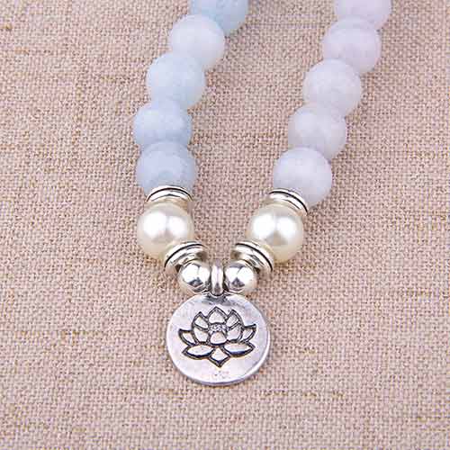 Bracelet mala 108 perles en aigue-marine avec symbole du lotus posé sur une nappe marron Kaosix