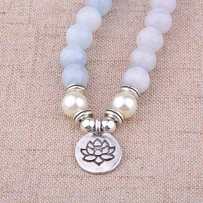 Bracelet mala 108 perles en aigue-marine avec symbole du lotus posé sur une nappe marron Kaosix