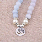 Bracelet mala 108 perles en aigue-marine avec symbole du lotus posé sur une nappe marron Kaosix