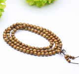 Bracelet mala tibétain bois santal 108 perles posé sur un sol blanc avec une laitue verte en fond Kaosix