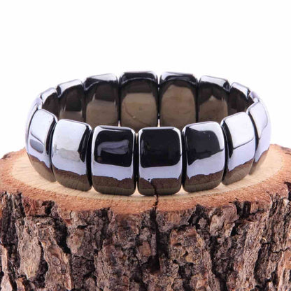 Bracelet pierres plates (plaquettes) obsidienne noire posé sur un tronc d'arbre coupé et un fond blanc Kaosix