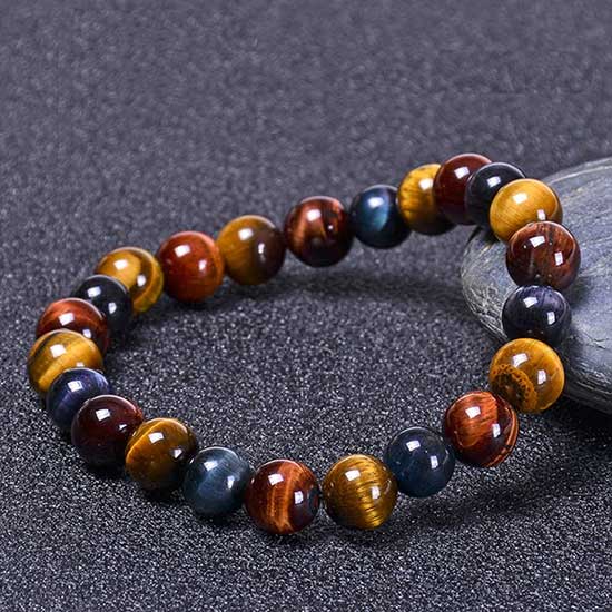 Bracelet triple protection œil de tigre œil de faucon et œil de taureau posé sur une pierre grise et sur un sol gris Kaosix