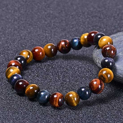 Bracelet triple protection œil de tigre œil de faucon et œil de taureau posé sur une pierre grise et sur un sol gris Kaosix