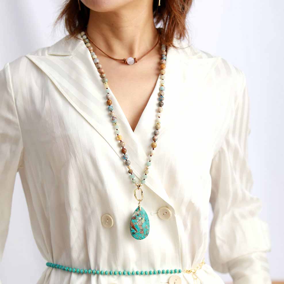 Buste de femme avec une veste blance et avec collier ras de cou perle quartz rose, un collier avec un pendentif en pierre verte et une ceinture de perles vertes Kaosix