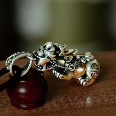 Collier Pendentif Feng Shui Pi Xiu Chance et Protection posé sur une table en bois vue de face Kaosix