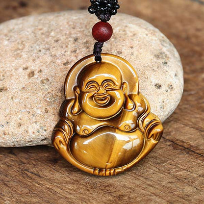 Collier pendentif Bouddha Rieur en Œil de Tigre posé sur une pierre blanche et sur une table en bois Kaosix