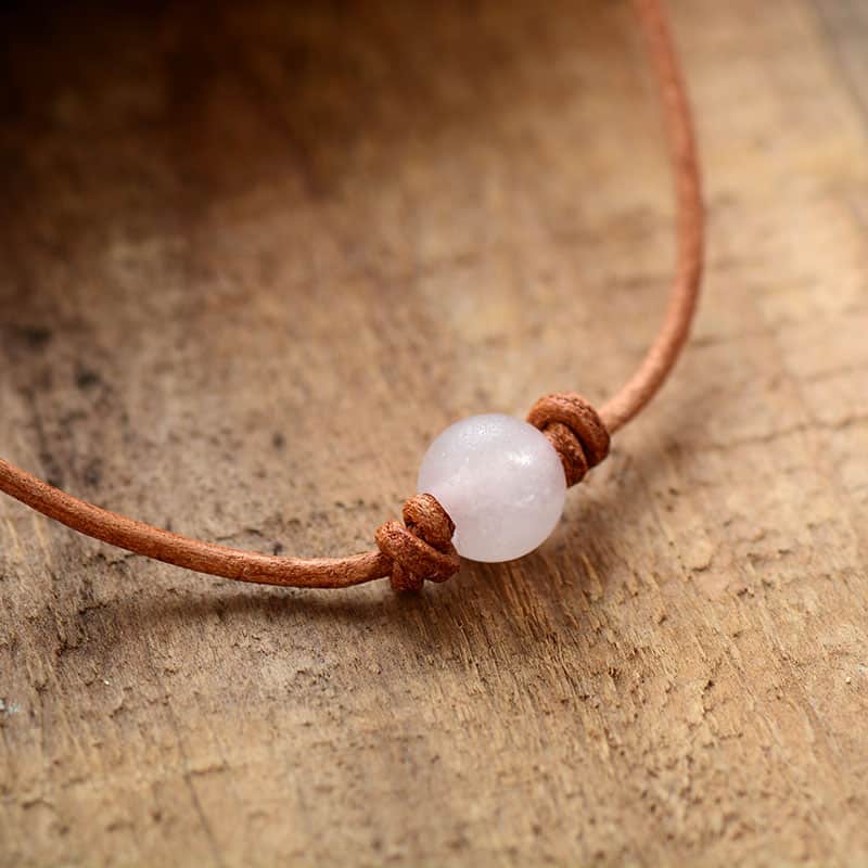 Collier ras de cou perle quartz rose en gros plan sur la perle et posé sur une table en bois Kaosix