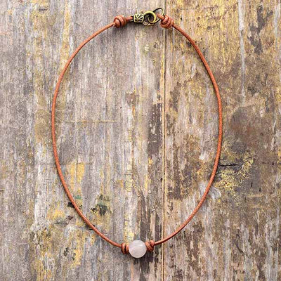 Collier ras de cou perle quartz rose posé sur une surface en bois
