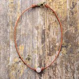 Collier ras de cou perle quartz rose posé sur une surface en bois