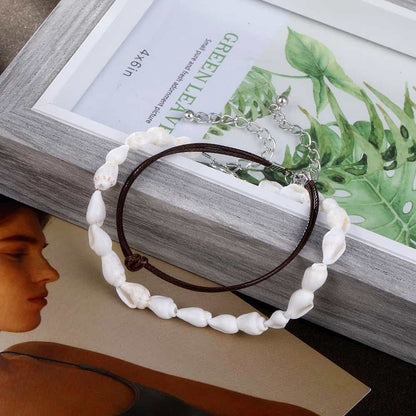Double bracelet de cheville en coquillages buccin et cordon de cuir posé sur un cadre de photo Kaosix