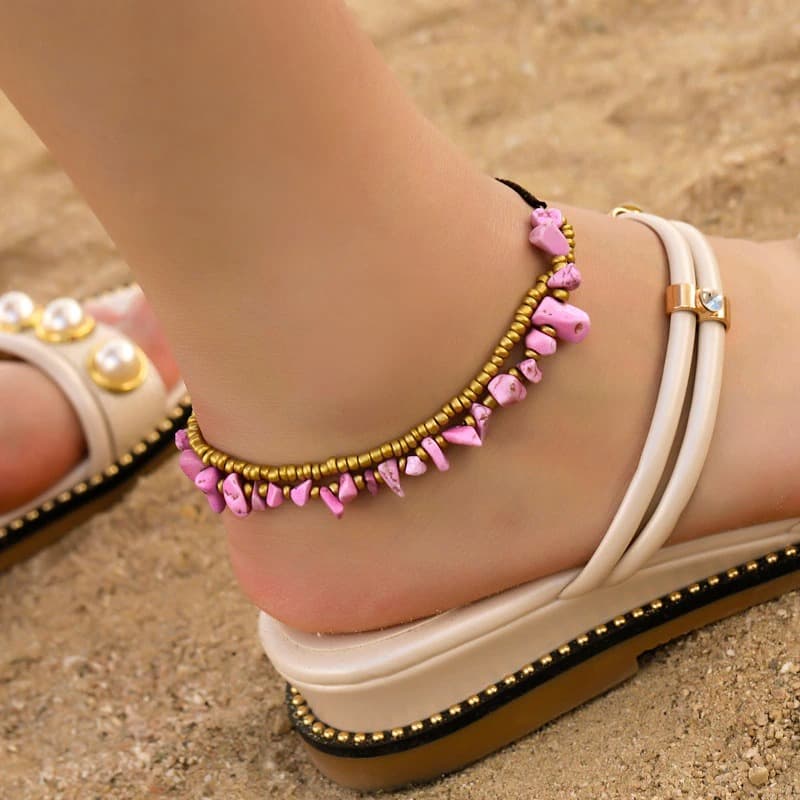 Double bracelet de cheville en éclats de tourmaline rose et perles de cuivre autour d'une cheville de femme portant des sandales Kaosix