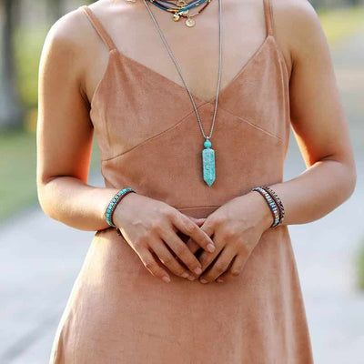 Jeune femme en robe marron portant un pendentif et plusieurs bracelets de pierres aux deux poignets Kaosix