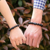La main d'un homme et la main d'une femme qui se tiennent par le petit doigt et qui chacun porte un bracelet obsidienne noire Dragon et Phénix au poignet Kaosix