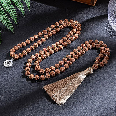 Mala 108 perles graines de Rudraksha Symbole Om (Aum) déroulé sur sol gris foncé Kaosix
