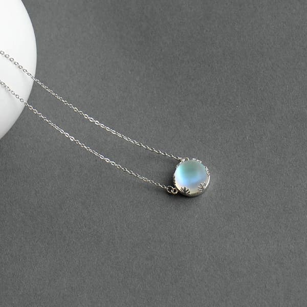 Pendentif Aurore Boréale perle de cristal bleu clair couronne argentée sur tapis gris Kaosix