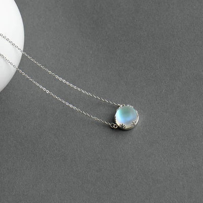 Pendentif Aurore Boréale perle de cristal bleu clair couronne argentée sur tapis gris Kaosix