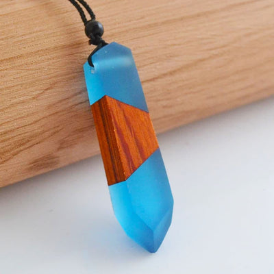 Pendentif (collier) en bois et résine bleue posé verticalement sur un socle en bois Kaosix