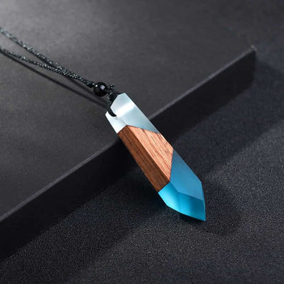 Pendentif (collier) en bois et résine bleue posé verticalement sur un socle noir Kaosix