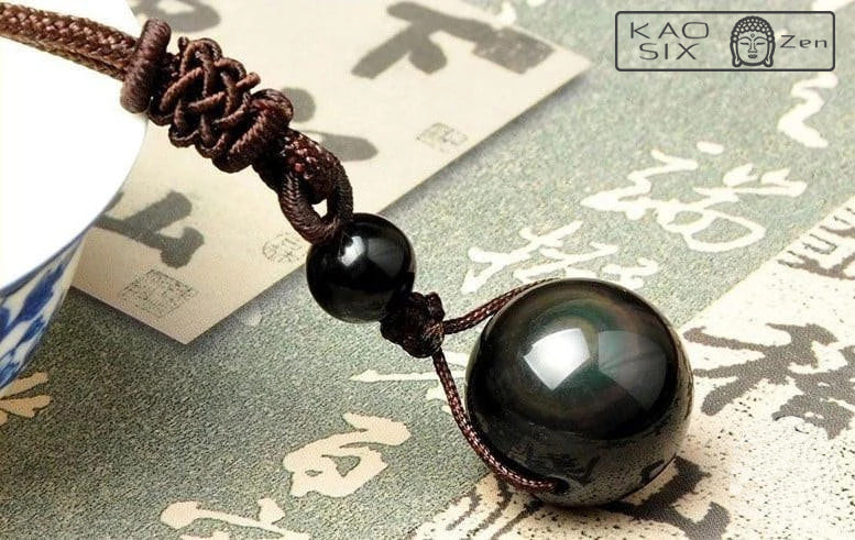 collier obsidienne œil céleste posé sur un bol en porcelaine et sur un tapis vert