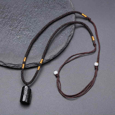 Pendentif tourmaline noire pierre brute pour homme posé sur une pierre grise plate et sur un sol gris Kaosix