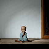 Petite statue moine bouddhiste salutation pose sur meuble en bois et sur fond blanc Kaosix